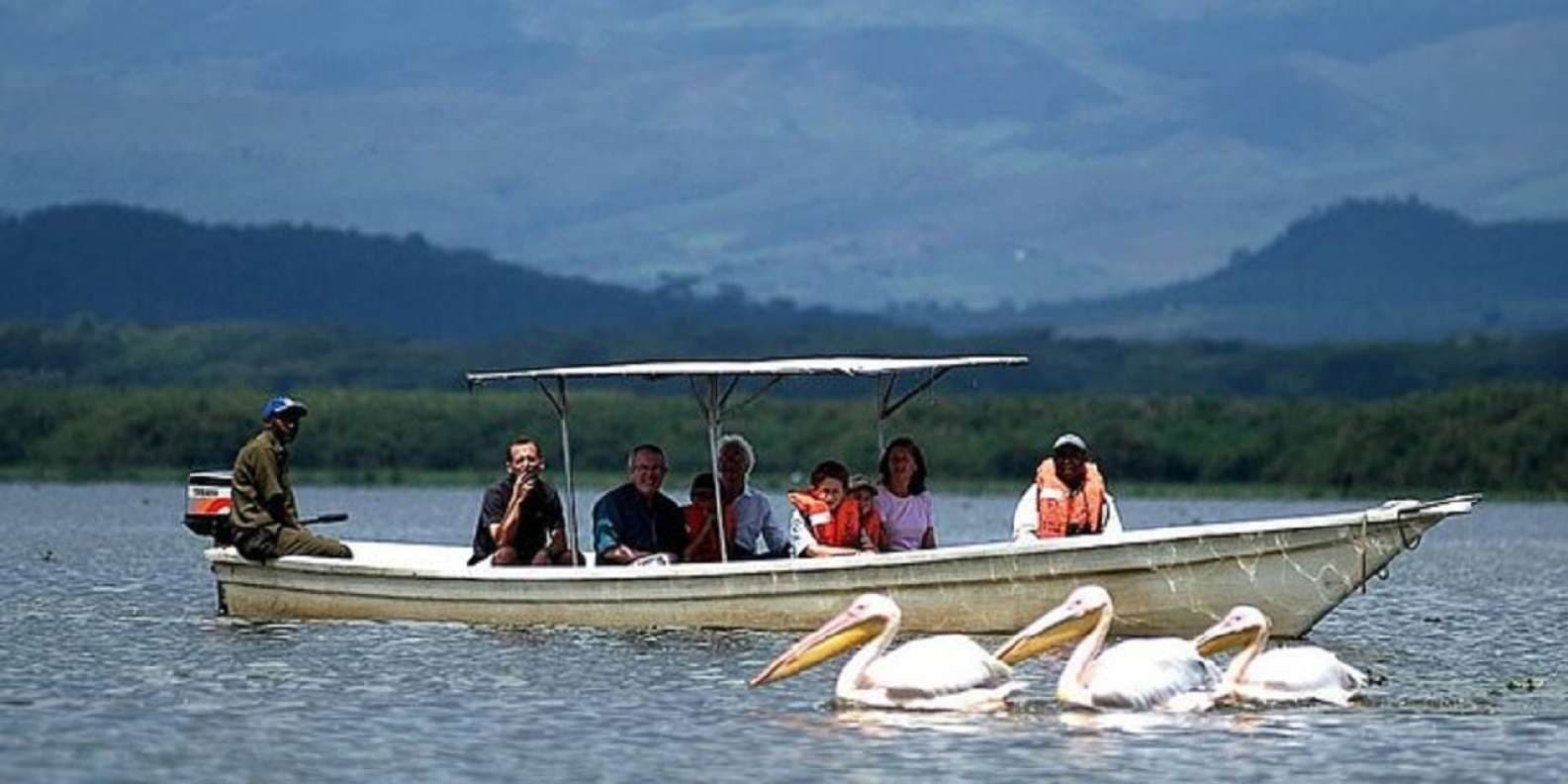 A small boat of passengers on Lake Naivasha with pelicans on the water