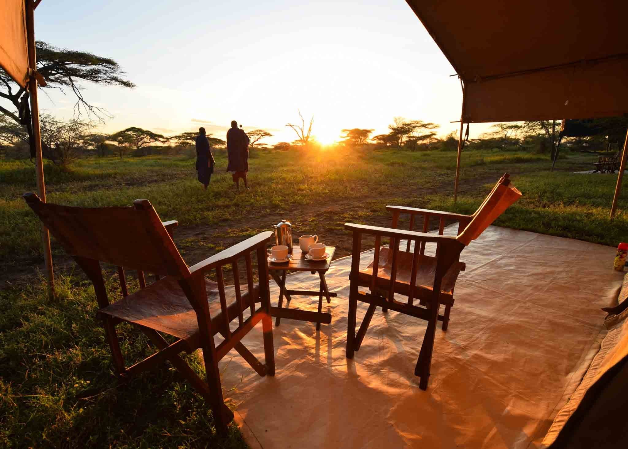A tented camp lit softly at dusk with the plains beyond