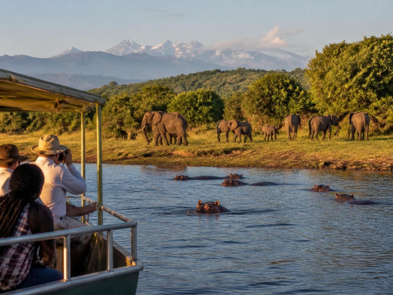 Boat on a channel with elephants and hippos at the water's edge